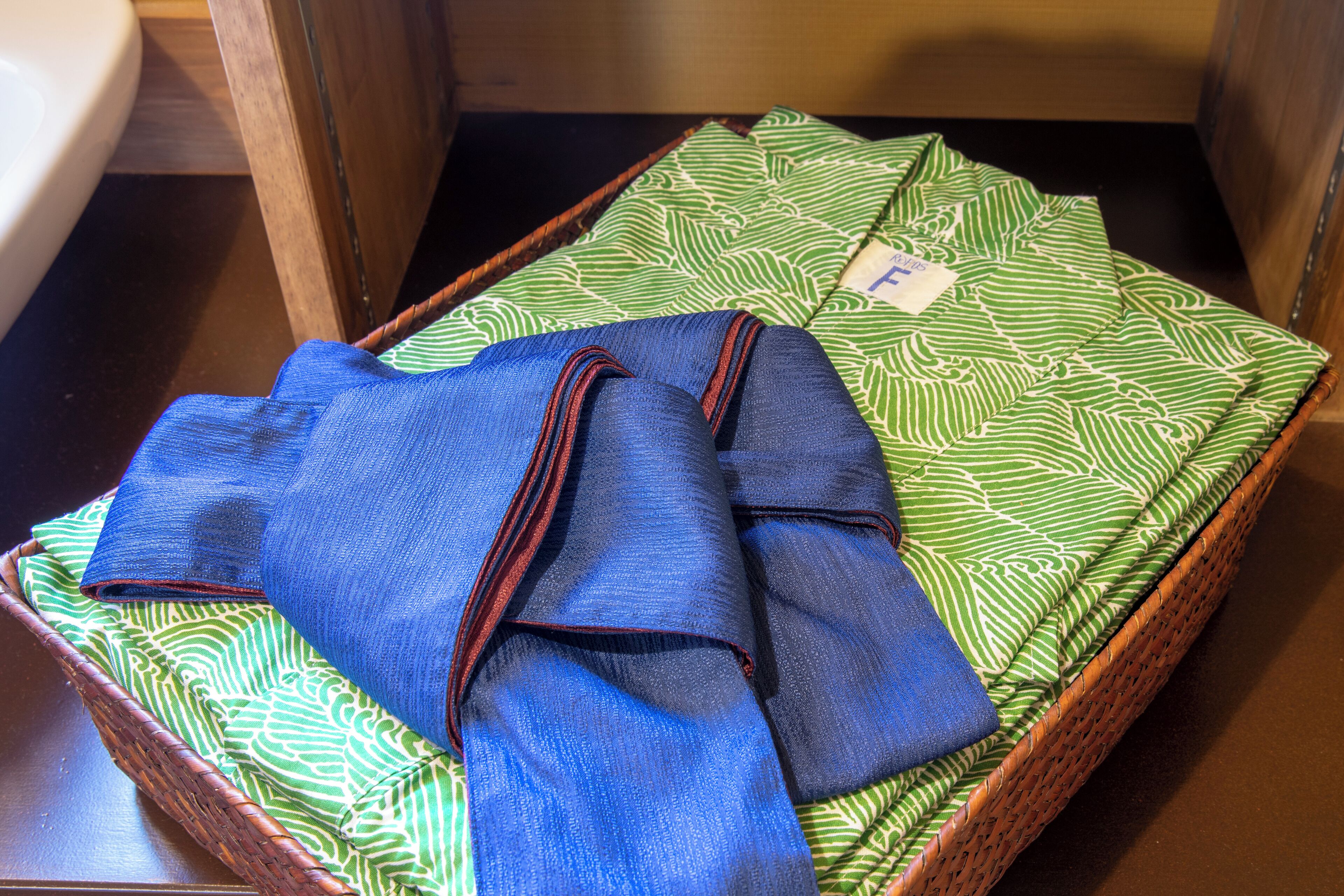 Una prenda azul doblada con cuidado sobre una tela verde estampada dentro de una cesta de mimbre.