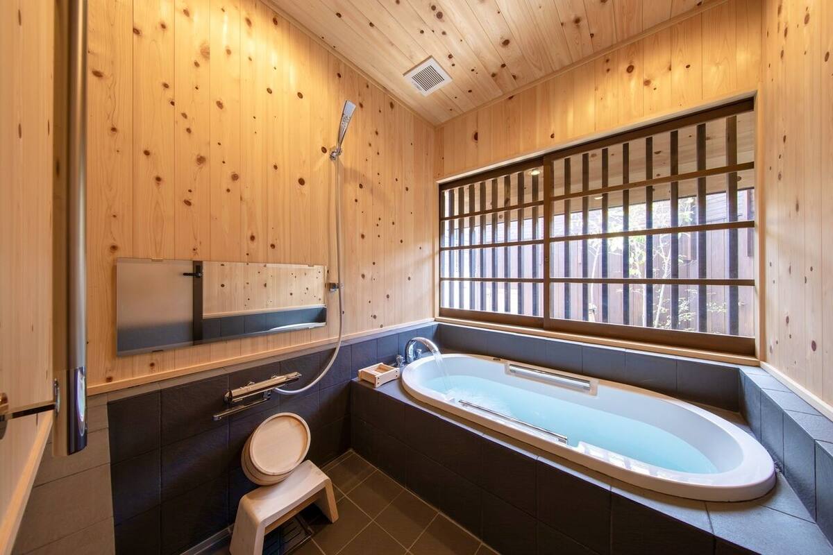 Ein Badezimmer mit Holzwandverkleidung, einer Badewanne, Toilette und einem Fenster.
