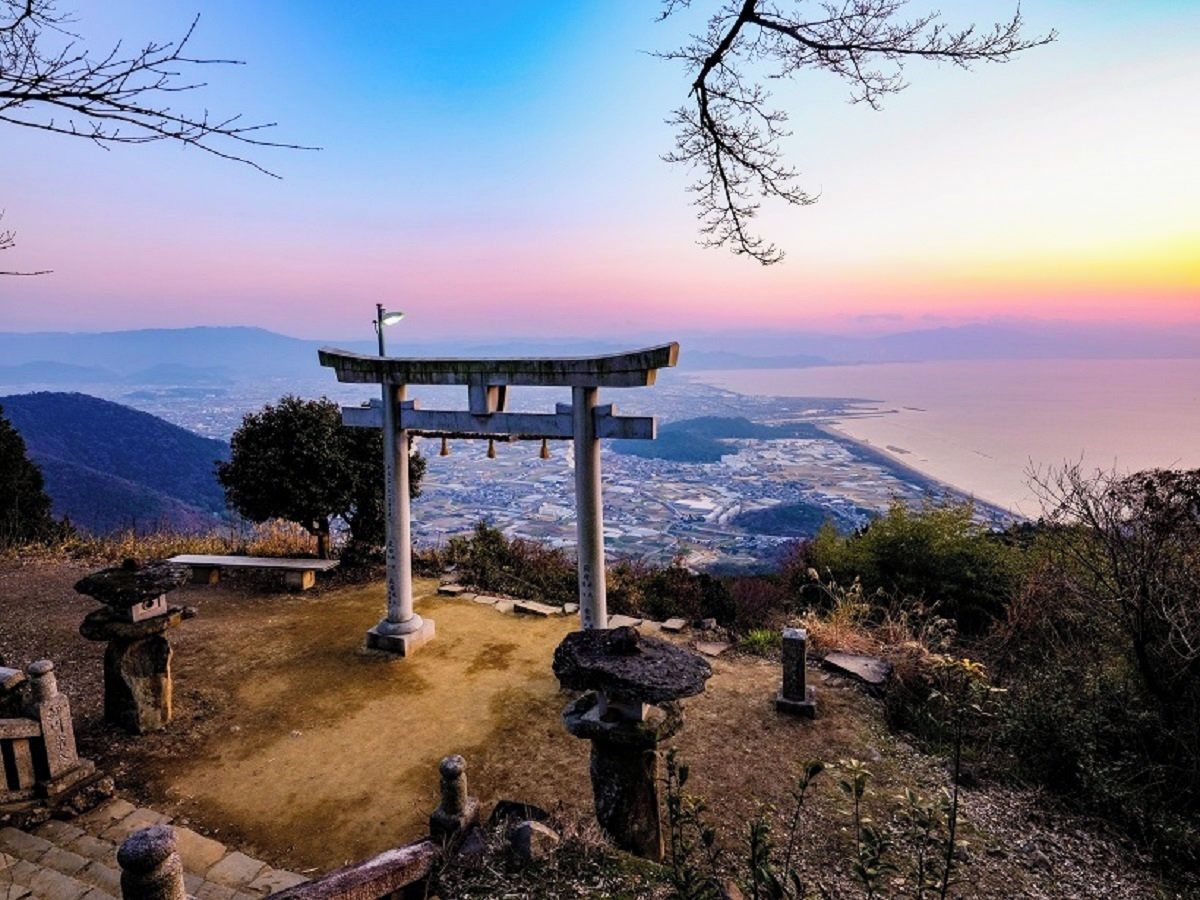 A traditional Japanese torii gate at the top of a hill overlooking a cityscape.