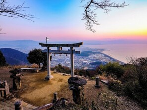 A traditional Japanese torii gate at the top of a hill overlooking a cityscape.