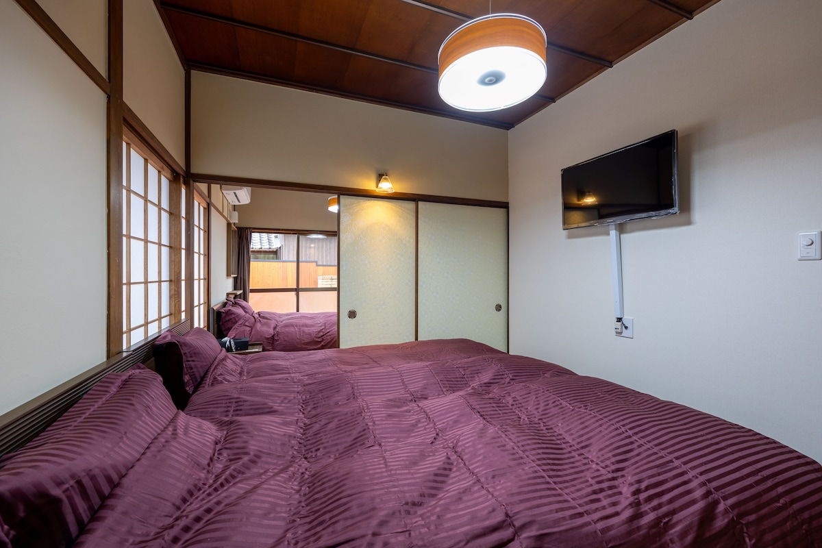 Een kamer met een groot bed, een aan de muur bevestigde televisie en schuifdeuren die naar een andere kamer leiden.
