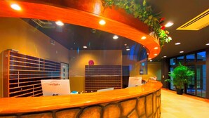 A reception area with a curved wooden counter, a clock, and a plant. - Glamping Cottage Liberty Resort Daito Onsen (Kakegawa)