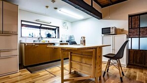 Una cucina con mobili in legno, un tavolo di legno e una sedia. Si vede una finestra sopra il lavello, un forno a microonde e un frigorifero.