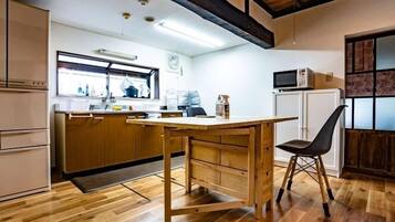 Una cocina con armarios de madera, una mesa de madera y una silla. Hay un ventanal sobre el fregadero, un microondas y un refrigerador.