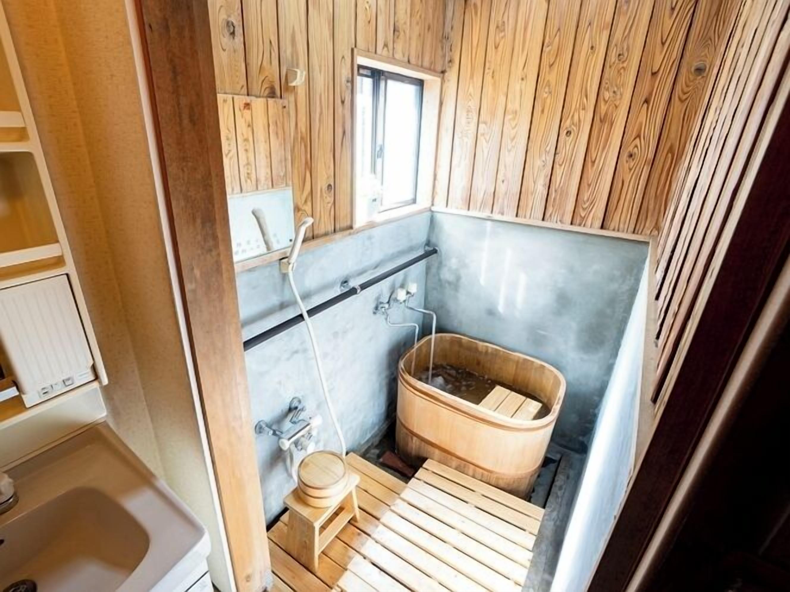 Un baño pequeño y acogedor con paredes y bañera de madera, además de un taburete de madera y una ventana.