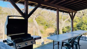 Un área de barbacoa al aire libre con una parrilla y una mesa bajo un pabellón de madera.