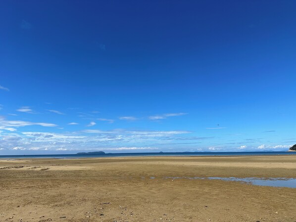 Una extensa playa de arena con cielo azul despejado y montañas a lo lejos.