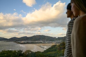 Un paisaje urbano costero con montañas al fondo, una playa y vistas de la ciudad desde un punto elevado.