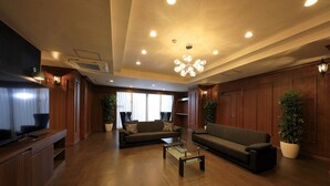 A spacious living room with a large sofa, a coffee table, and a television. There are potted plants and wooden paneling on the walls. - Tatami no Yado Chatan Mihama by Coldio Premium (Chatan)