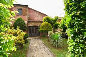 A stone pathway leading to a rustic house with a tiled roof, surrounded by well-maintained greenery and a neatly trimmed bush. - Villa mit Pool in Kaštelir für 9 Personen (Kaštelir)
