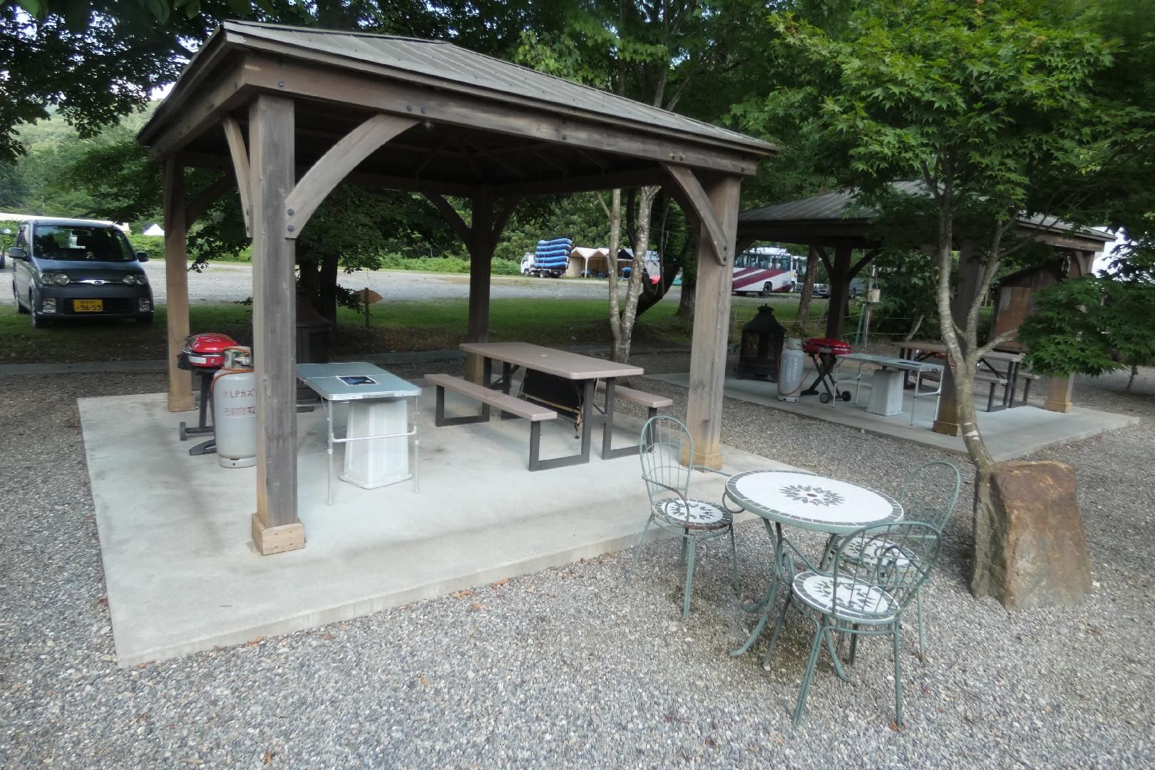 A covered picnic area with benches and tables, surrounded by trees.