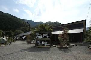 A sign for Minakami Campsite and River Stone, with a gravel path leading to a building with a sloped roof.