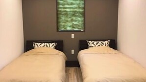 A room with two beds, a window with blinds, and a light fixture on the ceiling.