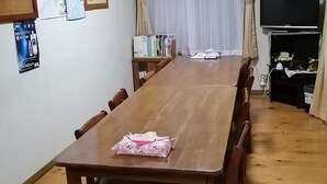 A dining area with a long wooden table, chairs, a TV, and an air conditioning unit. - Kujukurihama Shirako Youth Hostel (Shirako)