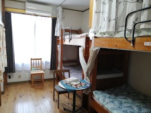 A compact room with bunk beds, a small table with a chair, and a window with curtains. - Kujukurihama Shirako Youth Hostel (Shirako)