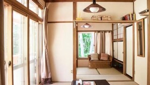 A traditional Japanese-style room with tatami flooring, a low table with a black tablecloth, a sofa, and a hanging lamp. - Hutte Lied (Komoro)