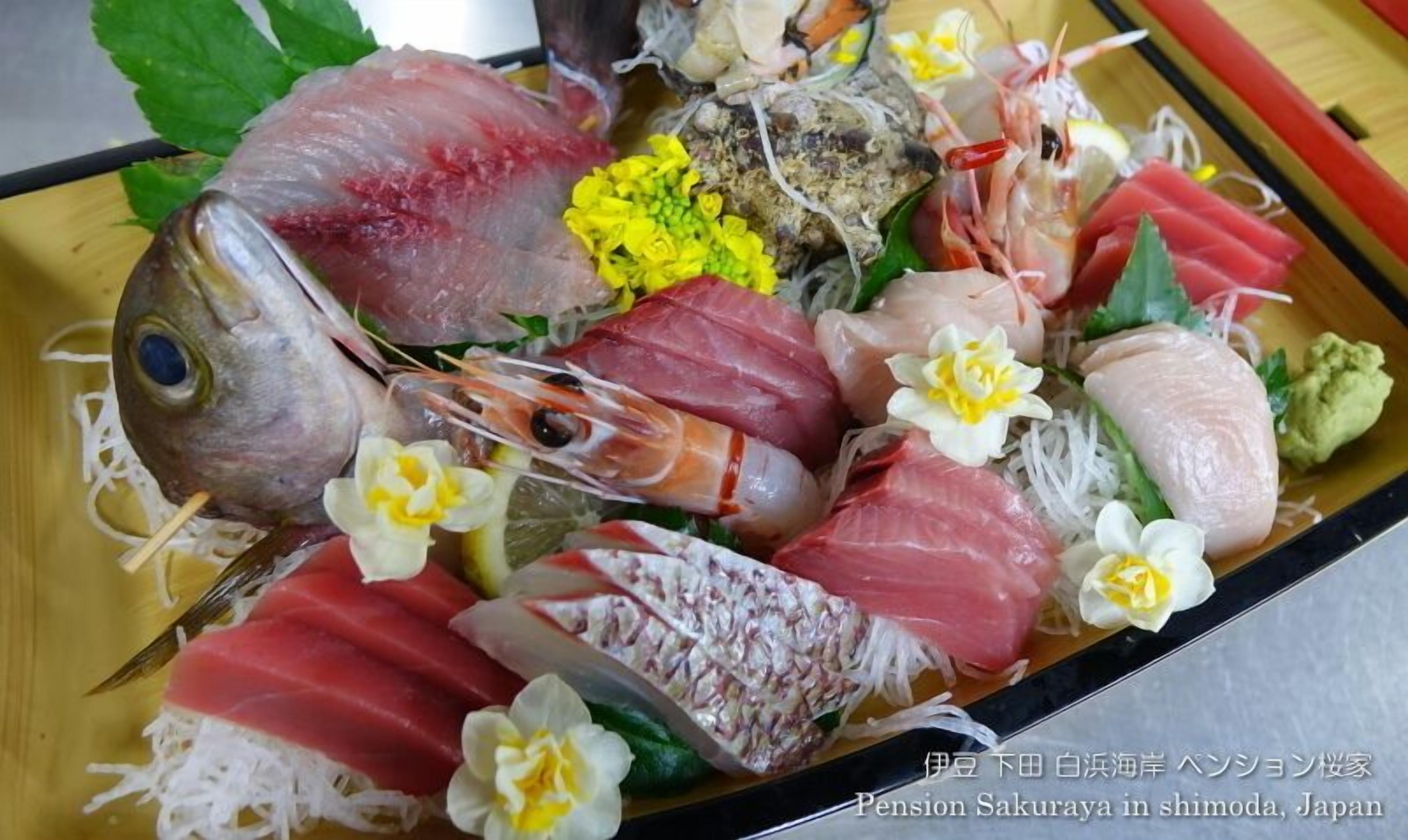 A variety of sashimi and sushi on a wooden tray, including fish, shrimp, and garnishes like wasabi and pickled ginger.