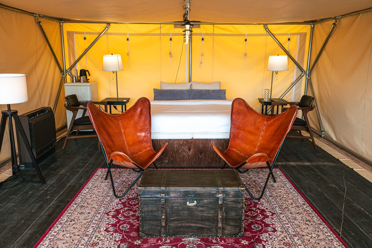 Een tent met een bed, twee stoelen, een tafel, lampen en een verwarming.