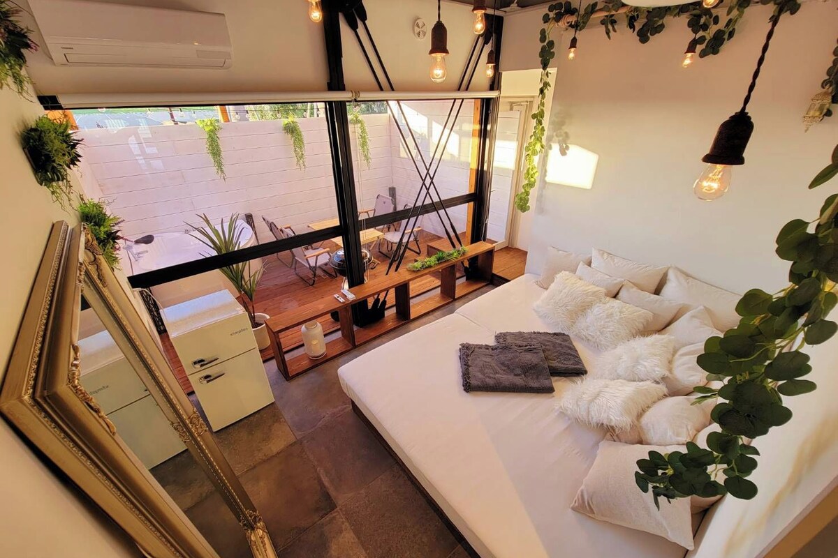 Een moderne slaapkamer met een groot bed, een houten bankje en uitzicht op de straat door grote ramen.