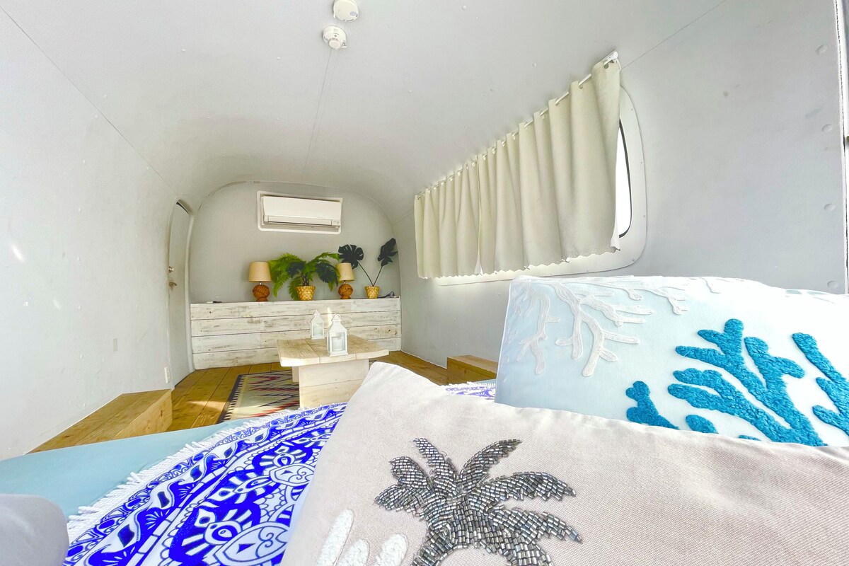 Een compacte, goed verlichte kamer met een bed, een klein tafeltje en een raam met gordijnen.