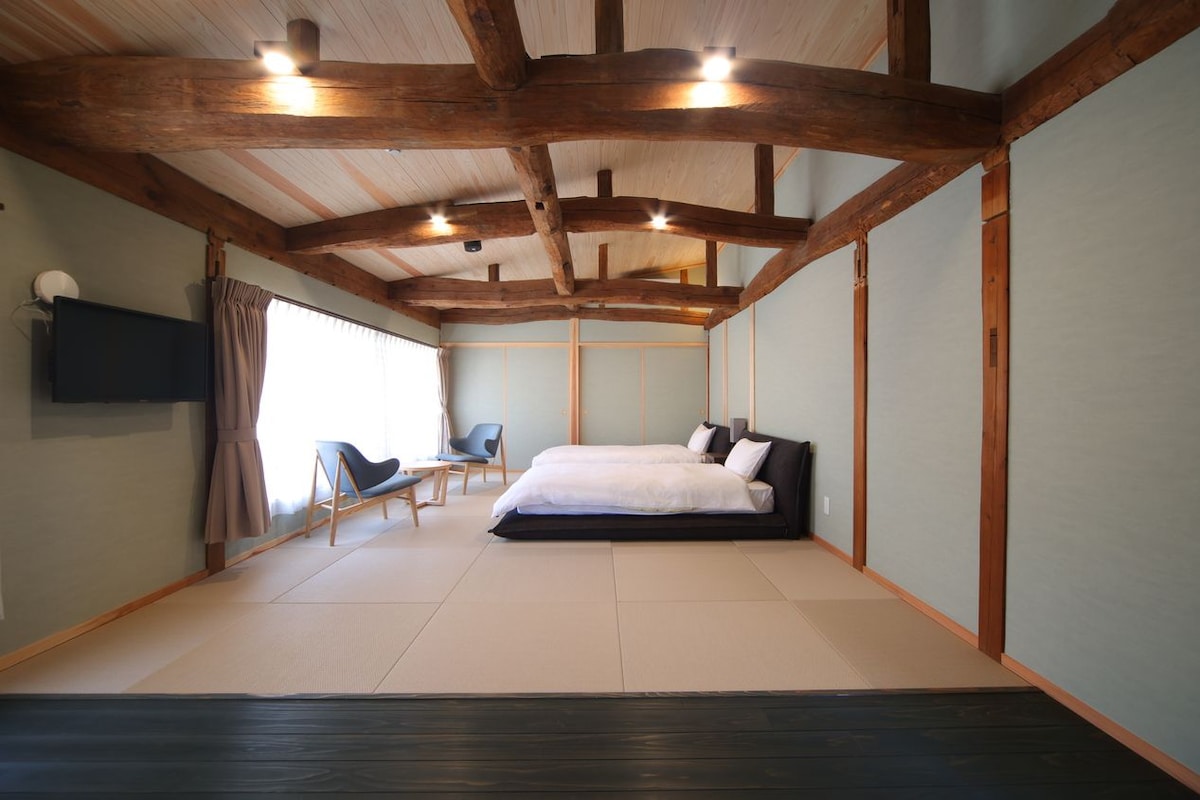 A bedroom with a wooden ceiling, a bed, a chair, and a TV on the wall.