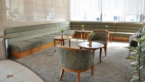 A modern lounge area with a green sofa, two wooden tables, and patterned chairs. - City Hotel Tomobe (Kasama)
