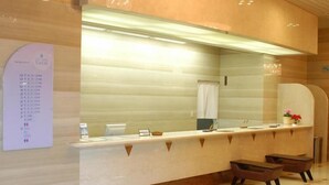 A reception area with a counter, a large mirror, a wall-mounted information board, and two chairs. - City Hotel Tomobe (Kasama)