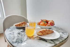 A marble table with croissants, a bowl of fruit, and two glasses of orange juice. - Cozy Apartment 1BR/3P - Ivry (Ivry-sur-Seine)