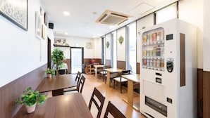 Een restaurant met houten tafels en stoelen, een automaat en potplanten.