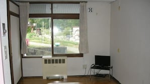 Una habitación con un ventanal grande, un radiador, un televisor sobre un mueble bajo y un futón en el suelo.