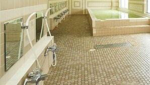 Un baño público con varios lavamanos, una bañera grande y piso de baldosas.
