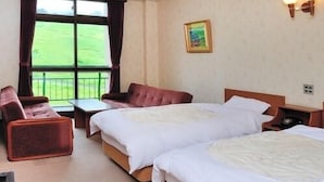 Habitación de hotel con dos camas, un sofá, una mesa y una ventana con vistas a un campo verde.
