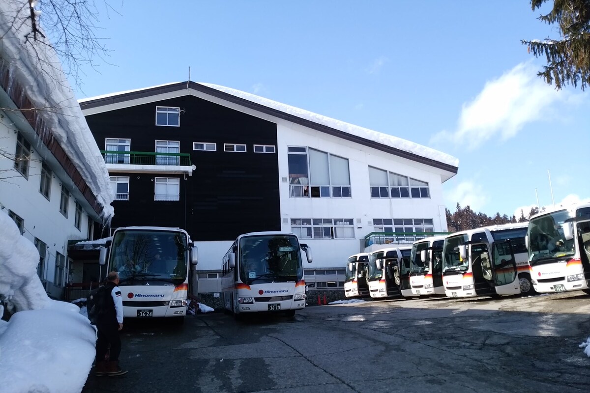 Un espace de stationnement où plusieurs autobus sont garés devant un bâtiment doté de grandes fenêtres et d’une façade noire et blanche.