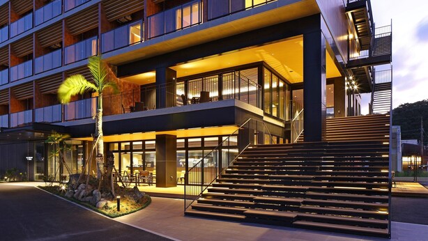 Un hôtel moderne à l’architecture à plusieurs niveaux, doté d’un espace extérieur aménagé et d’un escalier menant à l’entrée.