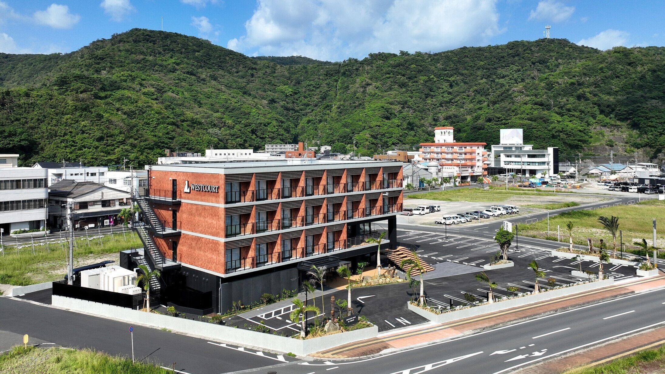 A modern building with a prominent 'Westcourt' sign, surrounded by a parking lot and a road with a mountain in the background.