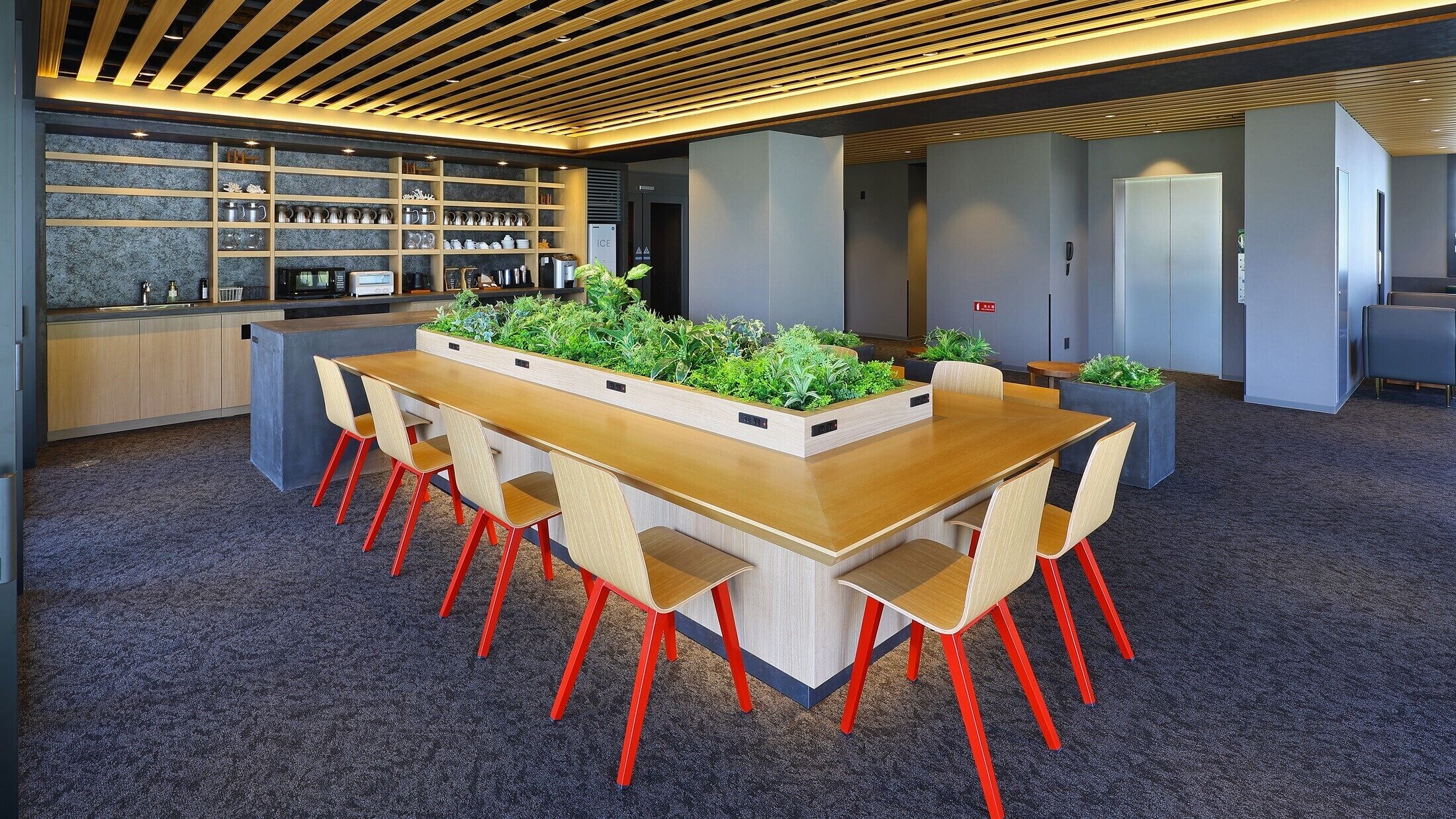 Une salle de réunion moderne, dotée d’une longue table en bois, de chaises rouges et d’un jardin intégré agrémenté de plantes vertes.