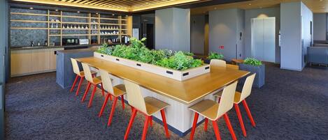 Une salle de réunion moderne, dotée d’une longue table en bois, de chaises rouges et d’un jardin intégré agrémenté de plantes vertes.