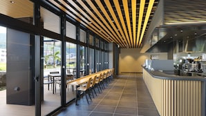 Un espace bar moderne doté d’un long comptoir, de sièges le long du mur et de grandes fenêtres offrant une vue sur l’extérieur.