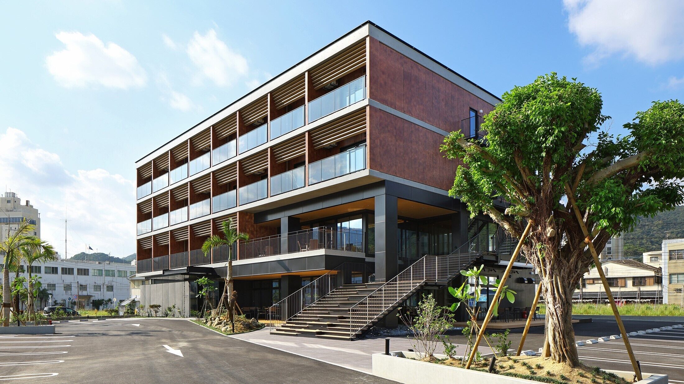 A modern multi-story building with a flat roof, large windows, and a staircase leading to the entrance.