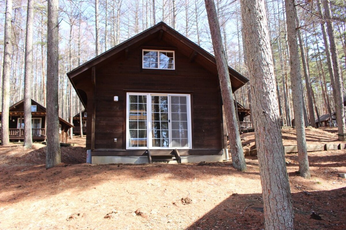 A rustic cabin with a large window and a small balcony, surrounded by tall trees.