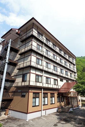 Un edificio de varios pisos con fachada plana, múltiples ventanas y una entrada visible con puerta y escalones.