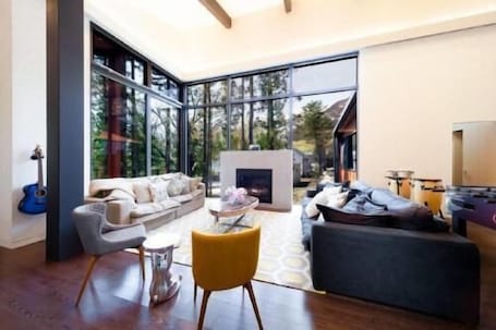 A modern living room with a fireplace, large windows, and a view of trees.