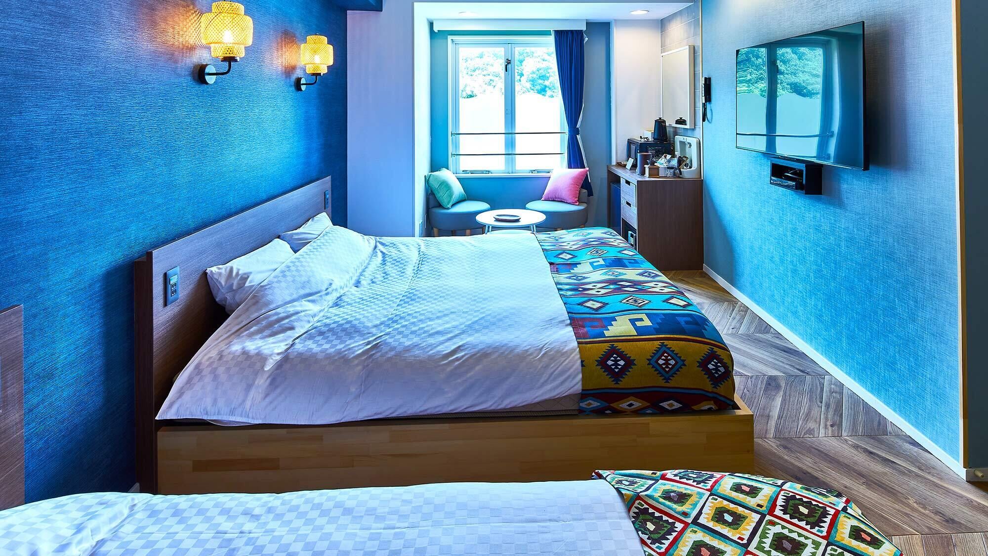 A hotel room with a bed, a small table, a chair, a TV, and a window with curtains.