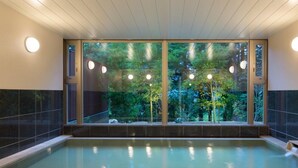 Une piscine intérieure moderne, dotée de grandes baies vitrées offrant une vue sur une zone boisée.
