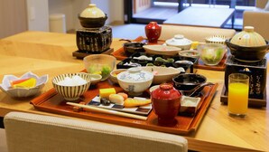 Une table à manger dressée avec divers plats japonais, un téléviseur et une vue sur l’extérieur.
