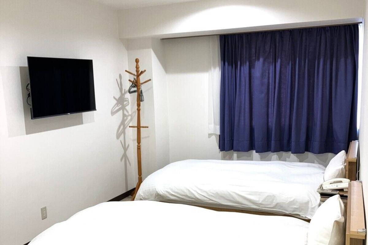 Un dormitorio con dos camas, un televisor montado en la pared, un perchero y una ventana con cortinas.