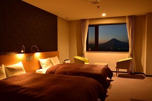 A hotel room with two beds, a desk, and a view of a mountain. - Fuji Yoko Hotel (Izu)