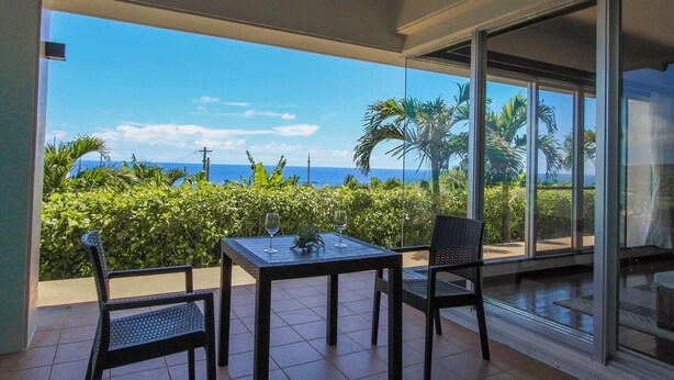 A balcony with a table and chairs, overlooking a tropical landscape with palm trees and the ocean. - Ryukyu Ritei Ingya (Miyakojima)