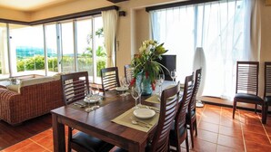 A dining area with a table set for four, surrounded by chairs, with a large window offering a view of greenery. - Ryukyu Ritei Ingya (Miyakojima)