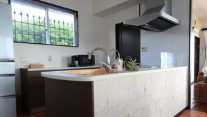 A modern kitchen with a central island, a microwave, a coffee maker, and a window with a view of greenery. - Ryukyu Ritei Ingya (Miyakojima)